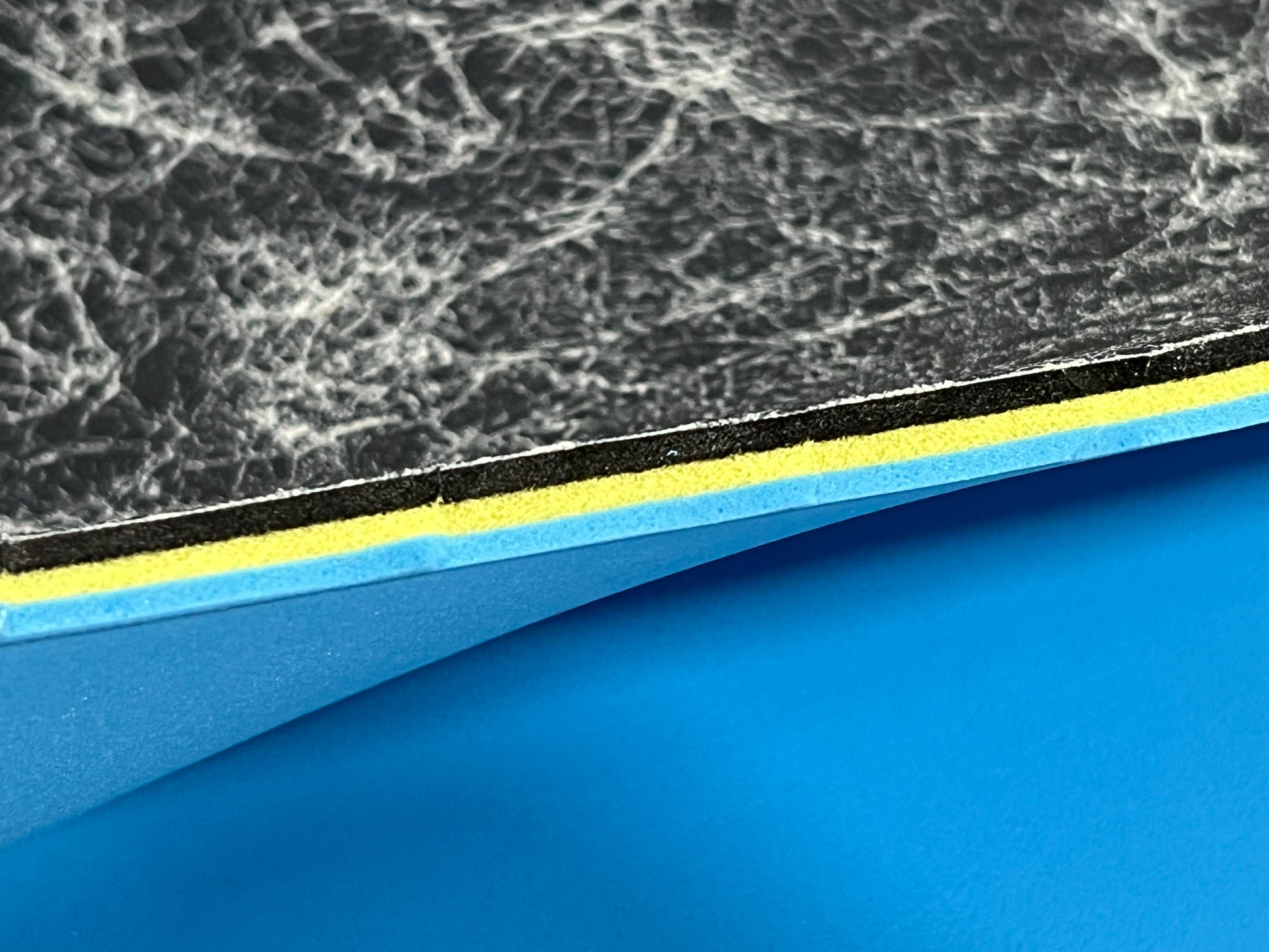 Close-up of textured edge of our 3/8" insole sheet which combines 3 different insole materials plus the Pure silver infused AG 2.0 topliner.
The composition is 1/8" Black Foam Fusion foam on top, then the 1/8" VeloShox foam in the middle with the 1.8" BounceBlu foam at the bottom.