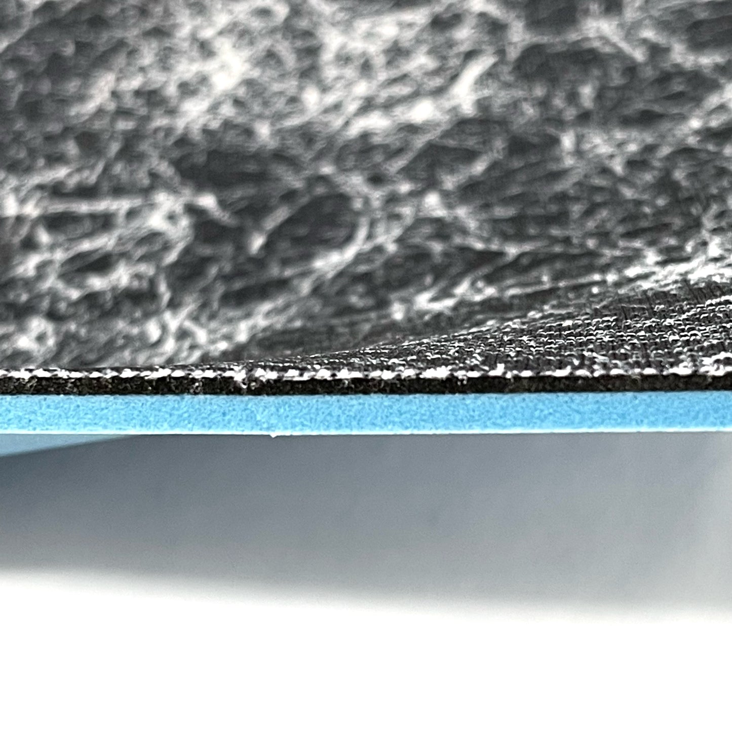 Side profile of insole sheet combination. You can see the silver infused black with silver pattern footbed on top and underneath that a thin 1/16" Black layer of FoamFuzion, then a 1/8" Blue layer of bounceBlue on a white background.