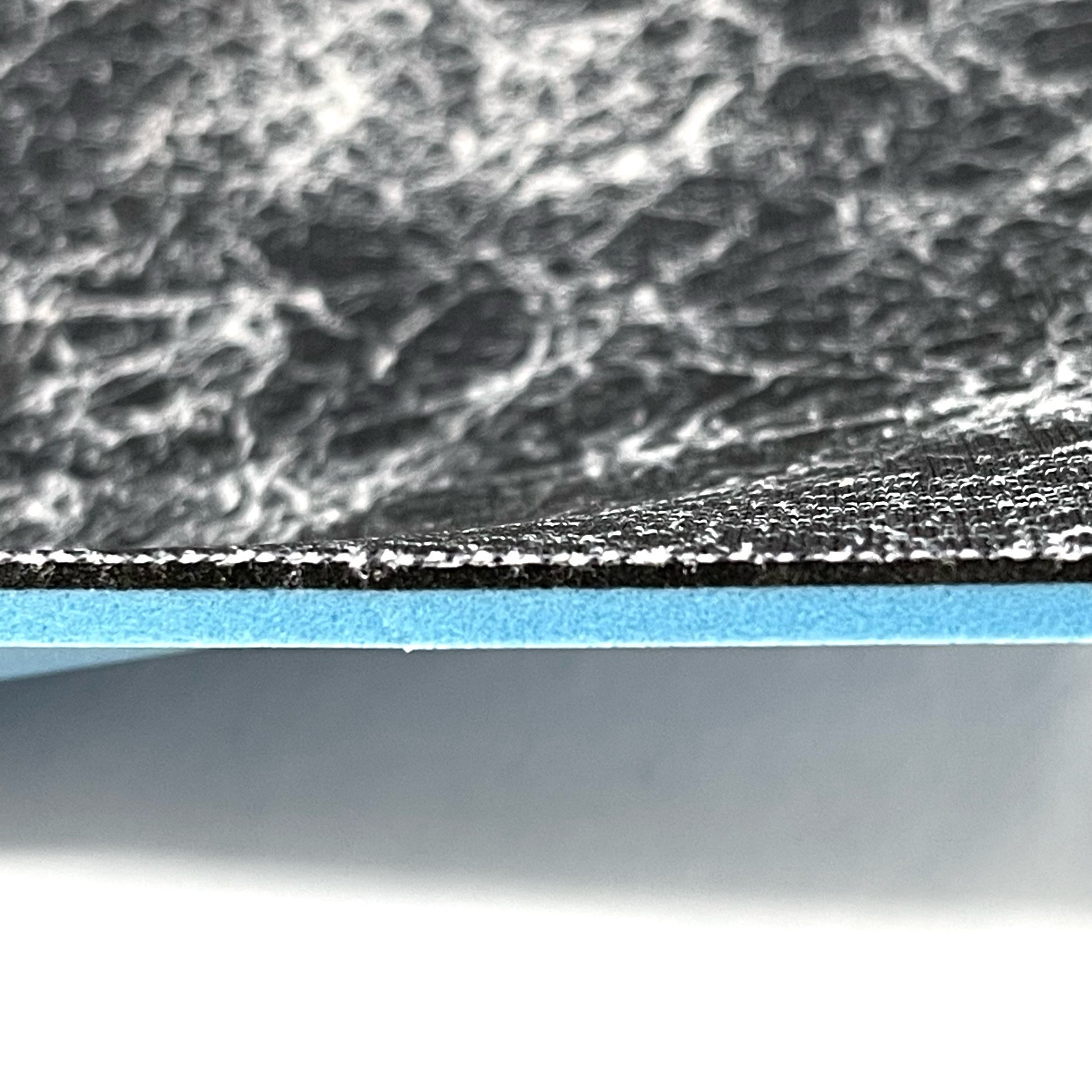 Side profile of insole sheet combination. You can see the silver infused black with silver pattern footbed on top and underneath that a thin 1/16" Black layer of FoamFuzion, then a 1/8" Blue layer of bounceBlue on a white background.